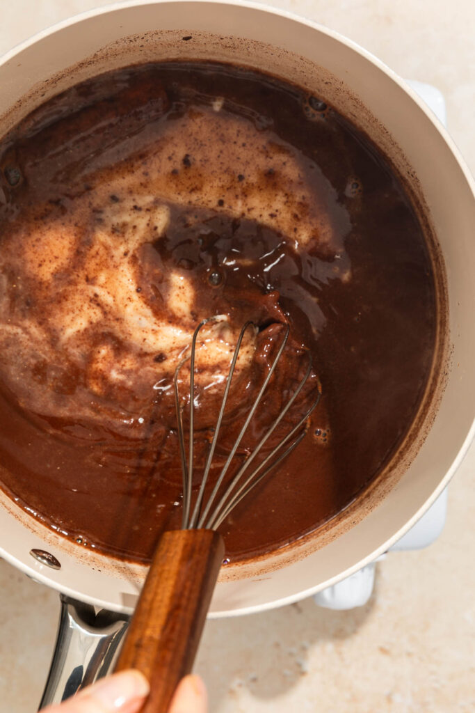 masa-harina being added to the champurrado chocolate mix in a saucepan
