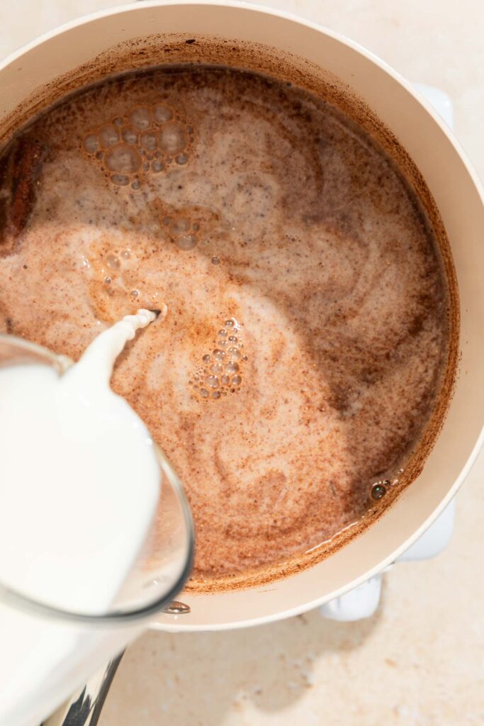 milk being added to champurrado mix in a small pot