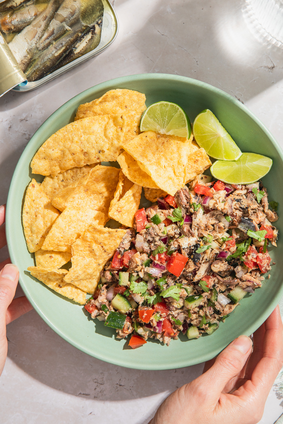 sardines ceviche served with tortilla chips and lime wedges with glass of water peaking into frame