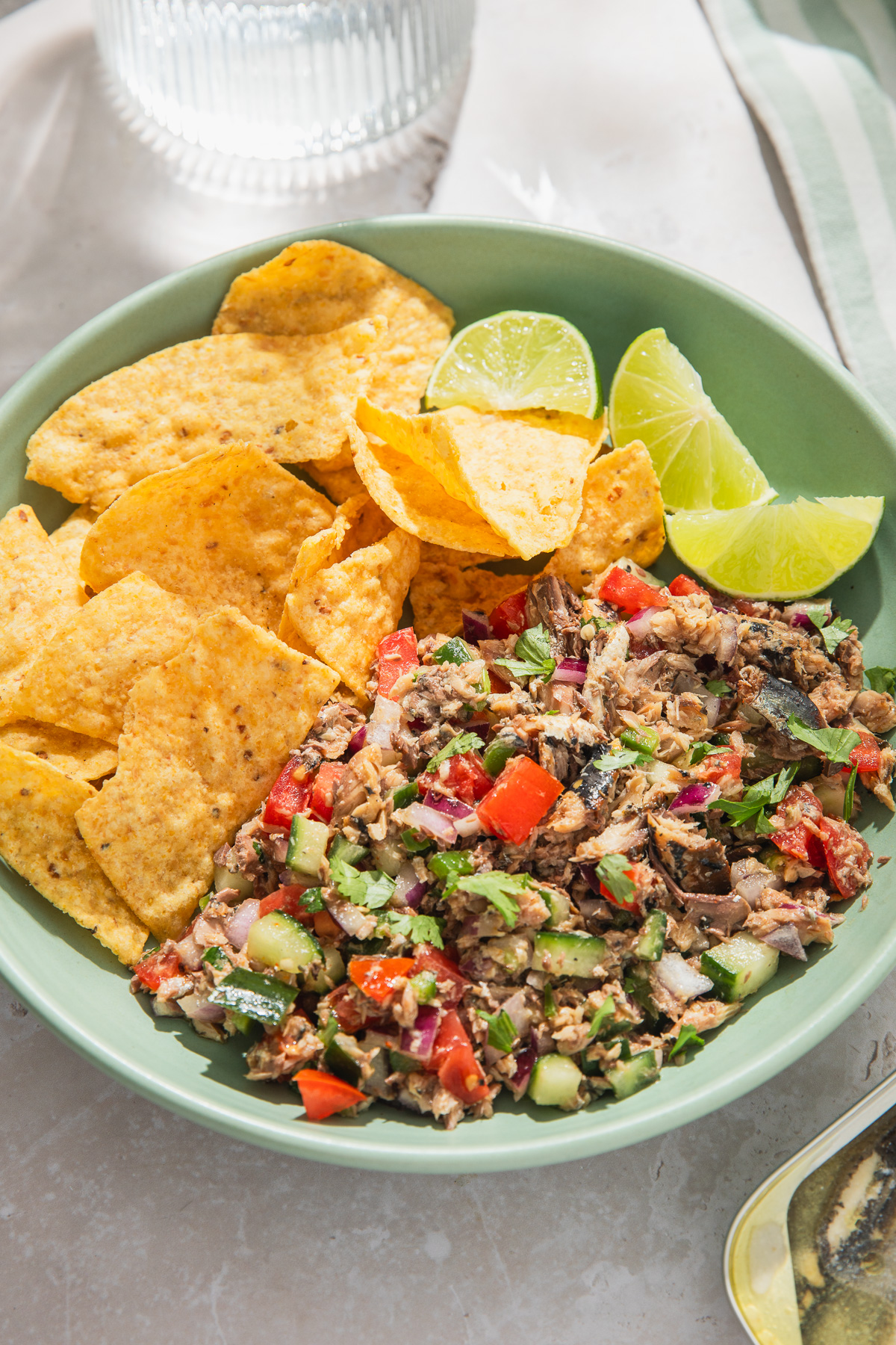 sardines ceviche served with tortilla chips and lime wedges with glass of water peaking into frame