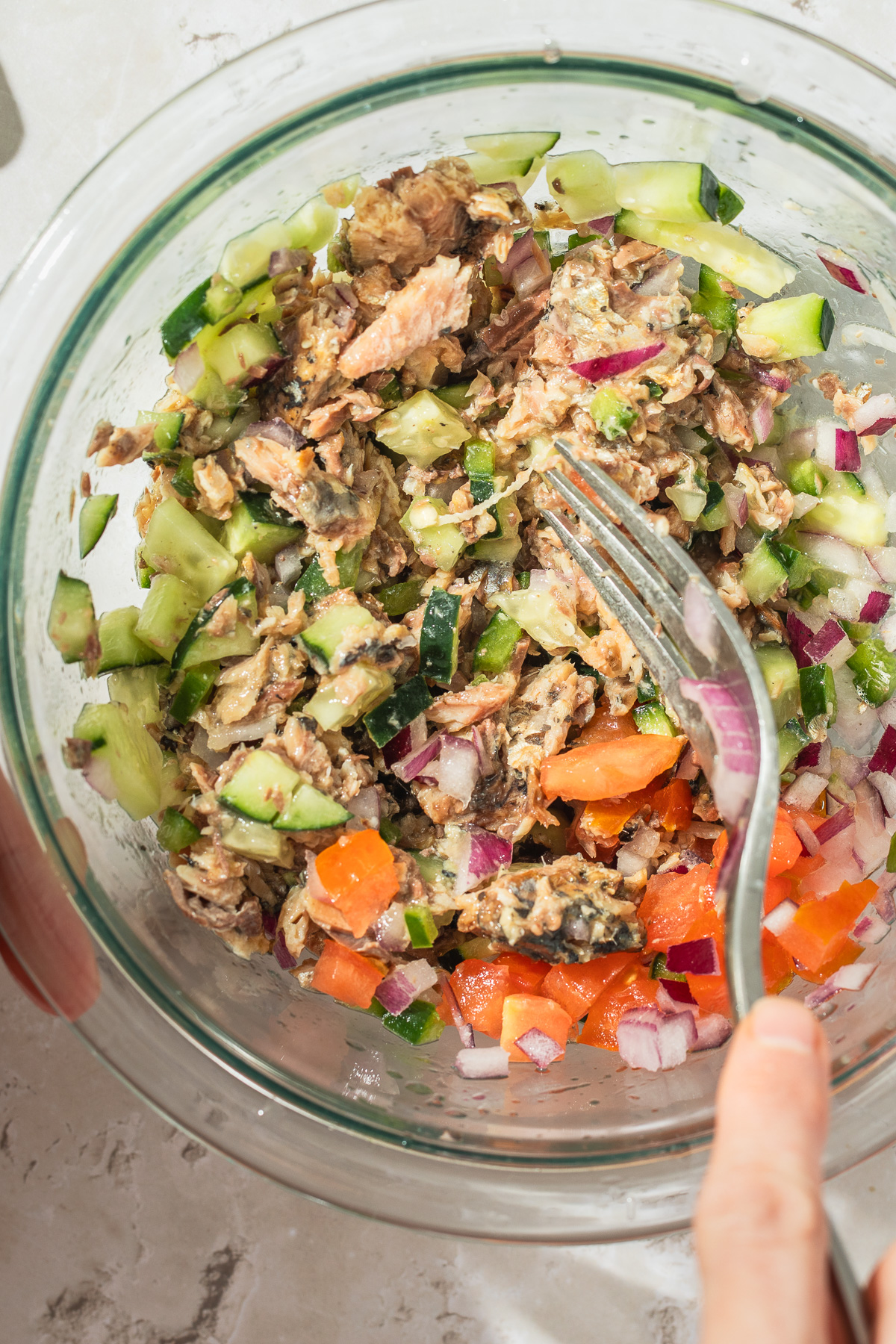 Sardine ceviche ingredients being combined on a glass blow with a fork